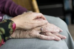A carer's hand over an elderly lady's hand