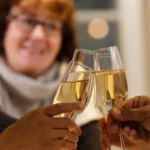 Three people clink glasses of champagne in a toast, with a smiling woman in the background, creating a warm and celebratory atmosphere.