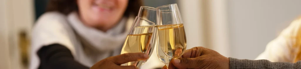 Three people clinking champagne glasses in a toast, with a smiling person in the background. The focus is on the glasses and hands in the foreground.
