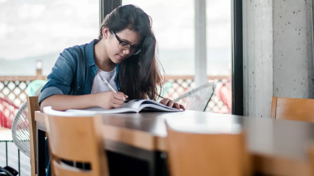 young adult student studying at desk and writing in book 16x9.
