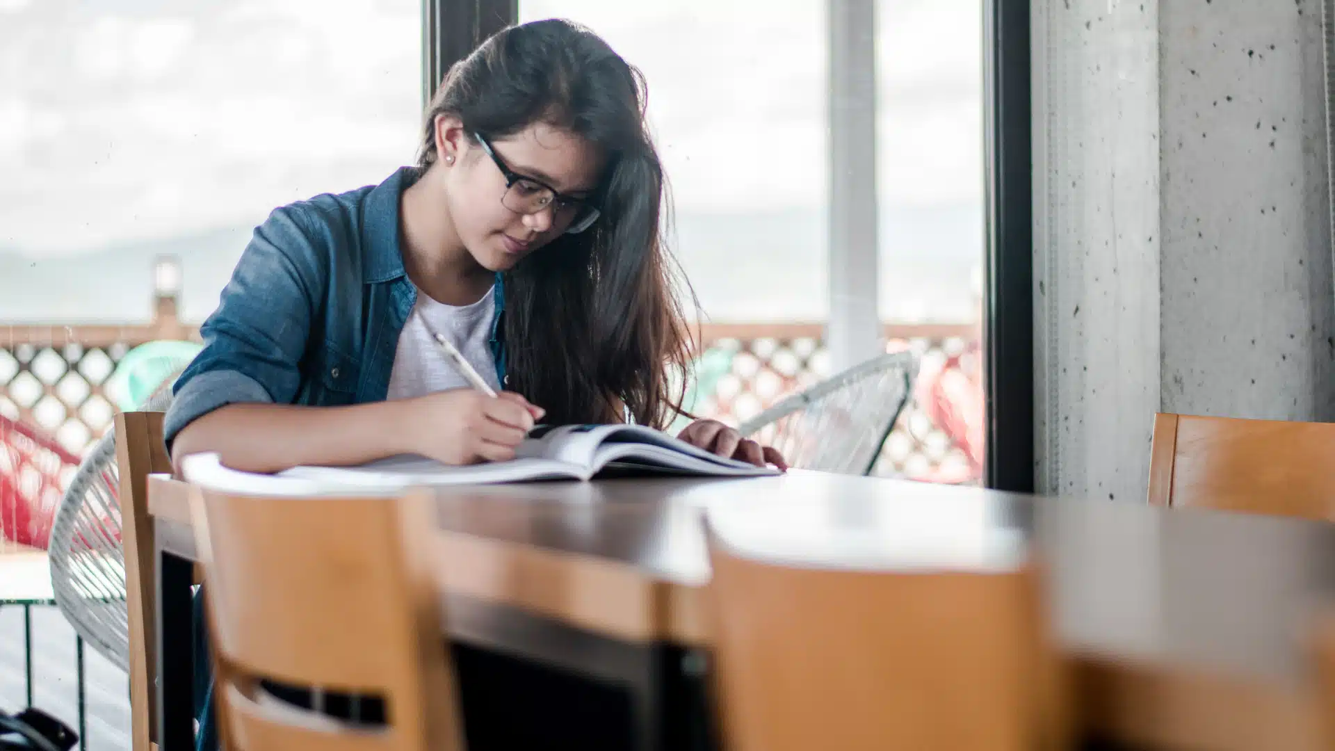 young adult student studying at desk and writing in book 16x9.