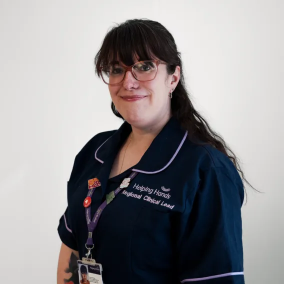A woman in glasses and a navy uniform with white trim, wearing a lanyard and badges, stands smiling against a plain white background.