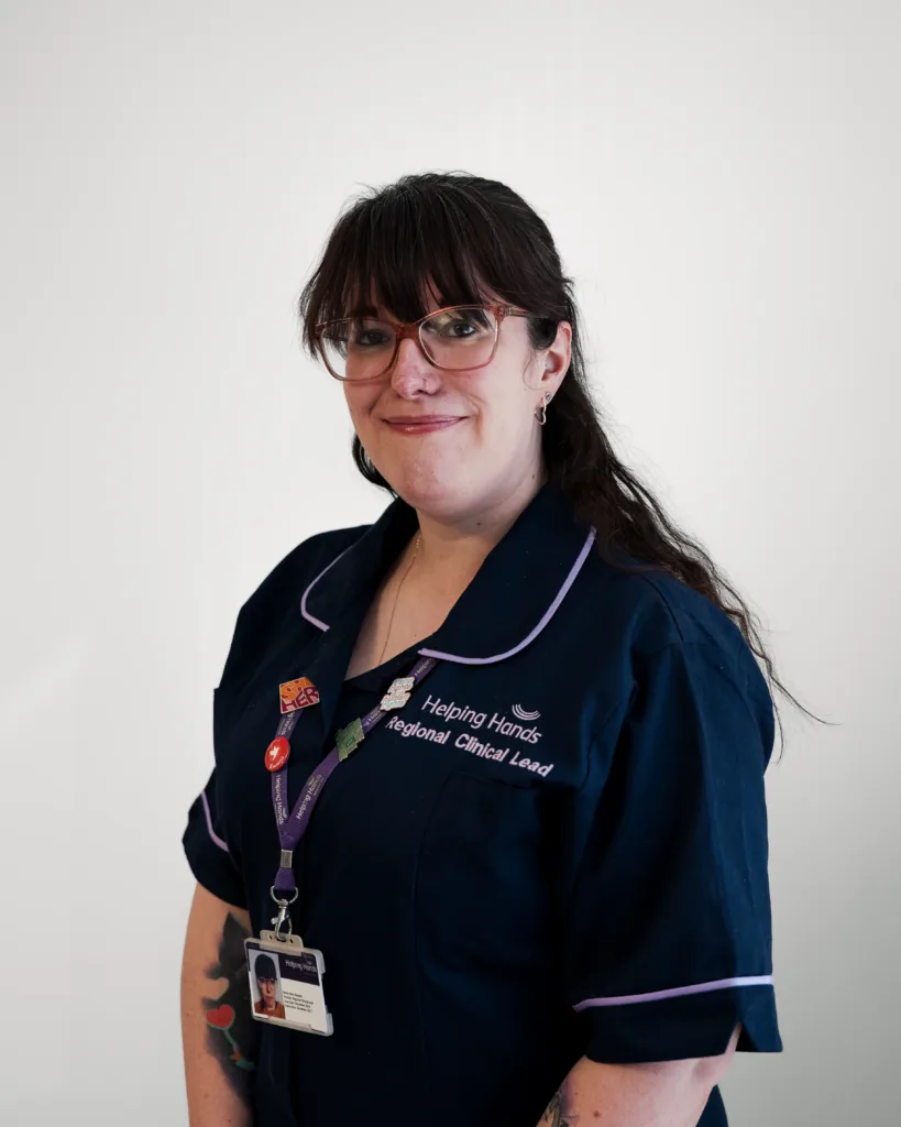 A woman in glasses and a navy uniform with white trim, wearing a lanyard and badges, stands smiling against a plain white background.