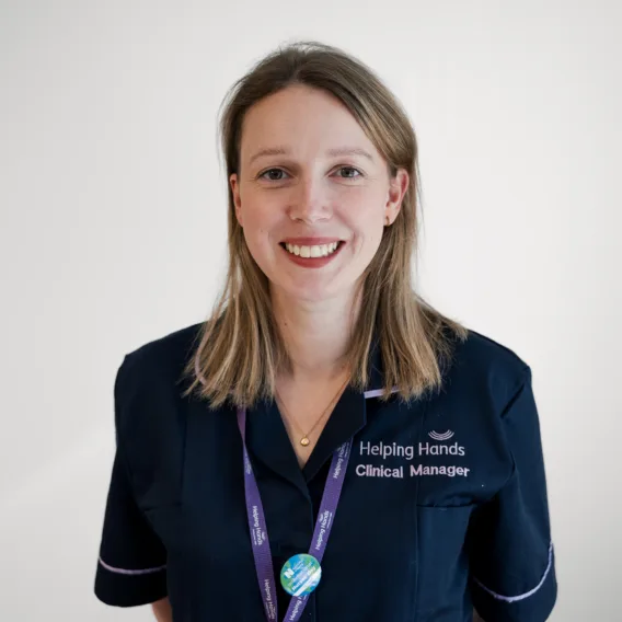 A woman in a navy blue uniform with Helping Hands Clinical Manager embroidered on it, wearing a lanyard and smiling at the camera against a plain white background.