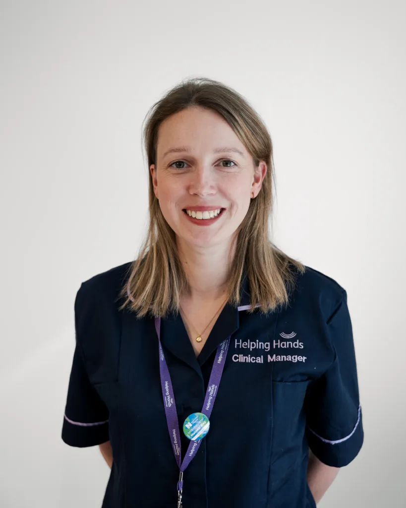 A woman in a navy blue uniform with Helping Hands Clinical Manager embroidered on it, wearing a lanyard and smiling at the camera against a plain white background.