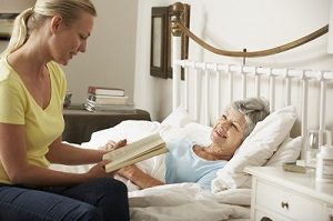 A carer reading to a lady in bed