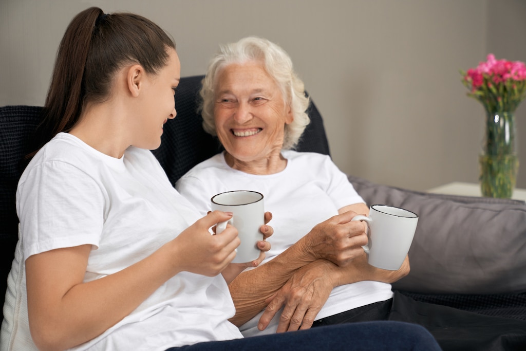 Elderly lady and live in carer smiling with a hot drink