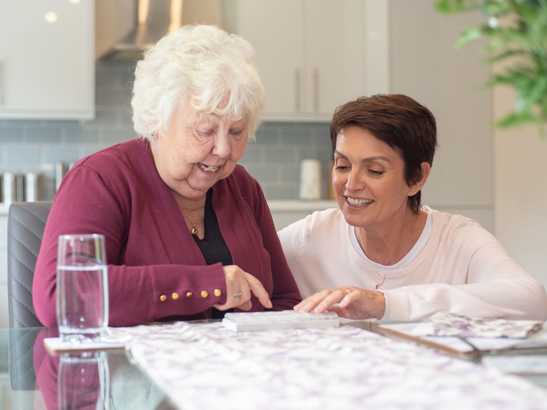 Elderly lady dining table dosette box glass of water female carer crouching down kitchen