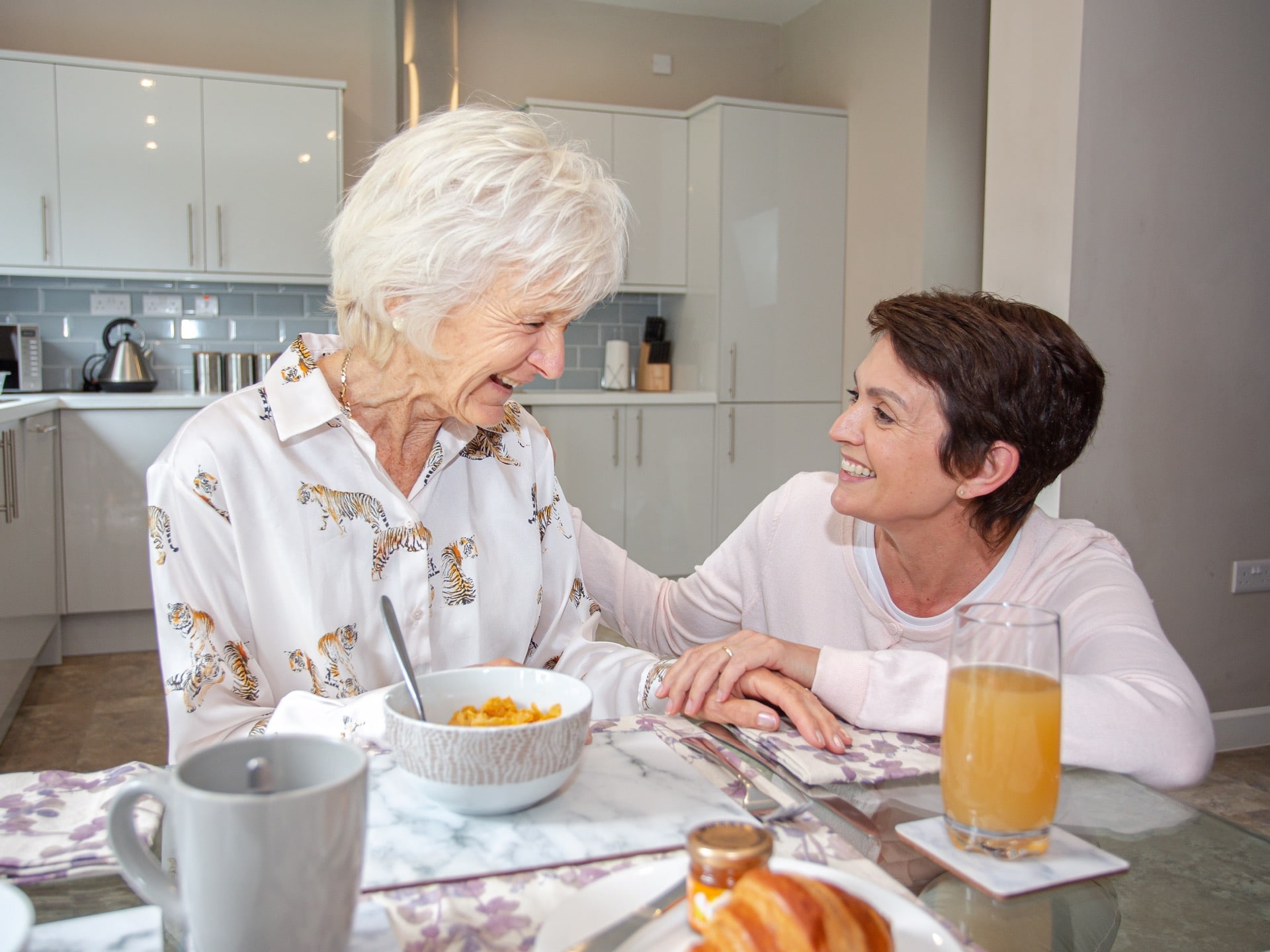 female-carer-crouching-beside-elderly-lady-tiger-printed-shirt-having-breakfast-smiling_4x3