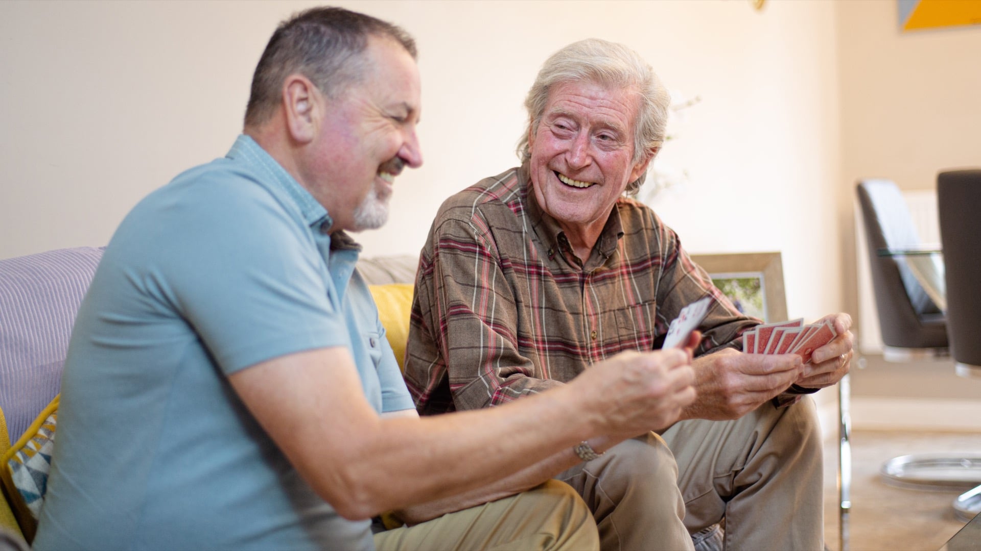 Male carer sitting on sofa elderly male playing cards